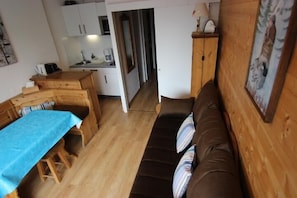 A cozy room with a wooden dining table, a brown sofa, and a kitchen area in the background.