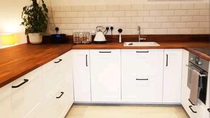 A kitchen with white cabinets, a wooden countertop, a sink, and a stove. - The Studio a Super Cute Place nr Southwold (Reydon)