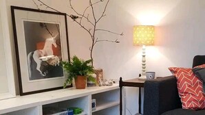 A living room with a sofa, a lamp, a framed picture, and a shelf with books and decorative items. - The Studio a Super Cute Place nr Southwold (Reydon)
