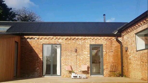 A brick building with two large glass doors, a small patio area with a table and chairs, and a metal roof. - The Studio a Super Cute Place nr Southwold (Reydon)