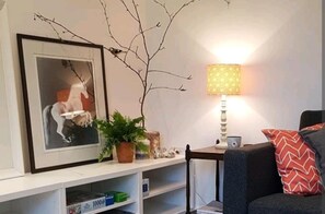 A living room with a framed picture on the wall, a lamp on a side table, a sofa, and a small shelf with items. - The Studio a Super Cute Place nr Southwold (Reydon)