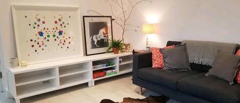 A modern living room with a grey sofa, a white entertainment unit, and a colorful abstract painting.