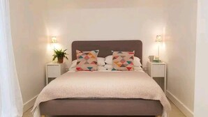 A neatly made bed with a patterned headboard, two bedside tables with lamps, and a small potted plant. - The Studio a Super Cute Place nr Southwold (Reydon)