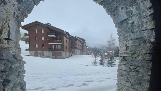 A snow-covered courtyard with a stone archway leading to a building with multiple balconies. - 200m from shops, view ski slopes, terrace, ski locker, 27m², Valmorel (Valmorel)