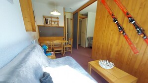A cozy room with a bed, a wooden table, a chair, a bookshelf, and skis leaning against the wall. - 200m from shops, view ski slopes, terrace, ski locker, 27m², Valmorel (Valmorel)