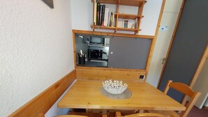 A small dining area with a wooden table and four chairs, a decorative white bowl on the table, and a bookshelf above the table. - 200m from shops, view ski slopes, terrace, ski locker, 27m², Valmorel (Valmorel)