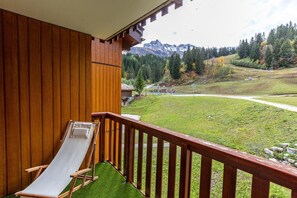 A wooden balcony with a lounge chair, a view of a mountainous landscape, and a grassy area. - Ski-in/ski-out & foot of the slopes, 1st floor, view ski slopes, balcony, ski locker, 27m², Valmorel (Valmorel)