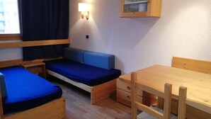 Une pièce compacte comprenant un lit superposé, un canapé-lit, une table en bois et une étagère fixée au mur.