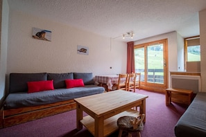 A cozy room with a sofa, a wooden table, and a chair. There is a window with a view of greenery outside. - 50m from shops, 2nd floor, view ski slopes, balcony, tv, ski locker, 33m², Valmorel (Valmorel)