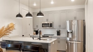 Une cuisine moderne dotée d’un îlot central, d’appareils électroménagers en acier inoxydable et de luminaires suspendus.