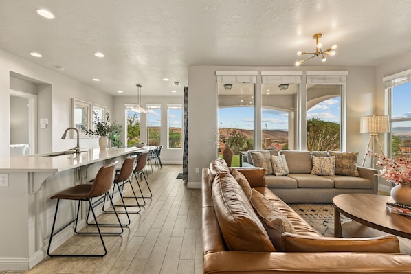 Una cocina moderna con barra, una zona de estar con sofá y sillones, y ventanas amplias que ofrecen vistas al exterior.