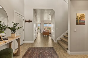 Un pasillo con piso de madera, un banco, una mesa con una planta y una puerta.