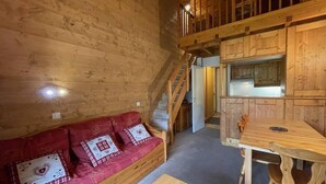 Interior de una cabaña de madera con sofá, una mesa de comedor y una escalera.