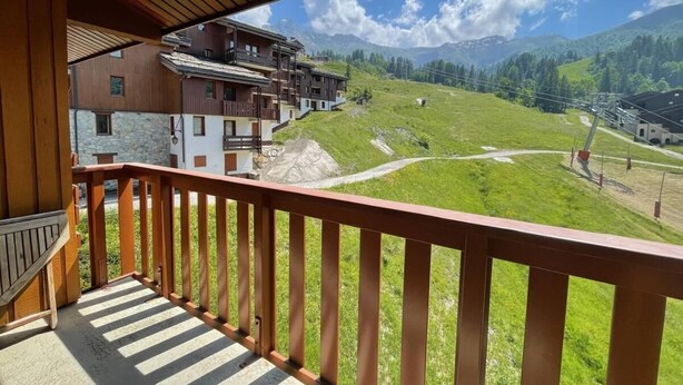 Un balcón de madera con vistas a un paisaje montañoso, un edificio de piedra y un telesilla.