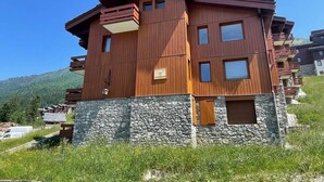 Un edificio de madera de varios pisos con balcones, cimientos de piedra y una vista despejada del paisaje circundante.