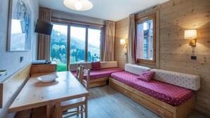 A cozy cabin room with a wooden interior, a dining table, two cushioned seating areas, and a television mounted on the wall. - 200m from ski slopes, floor -1, view ski slopes, terrace, tv, ski locker, 21m², Valmorel (Valmorel)