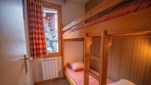 A bunk bed room with a window, a radiator, and a door.