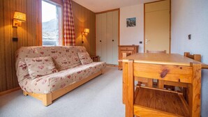 A cozy room with a sofa, wooden dining table, and a view of a mountain.