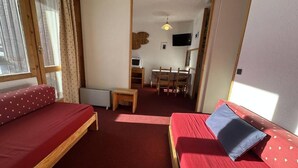 A cozy room with two red beds, a small wooden table, and a TV in the background.
