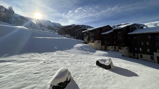 A snow-covered mountain path leading to a row of chalet-style buildings with balconies, under a clear sky.