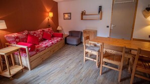 A cozy room with a wooden sofa, a dining table, and chairs. There is a small table and a chair near the sofa. - Ski-in/ski-out & foot of the slopes, 3rd floor, view ski slopes, balcony, tv, ski locker, 36m² (Valmorel)