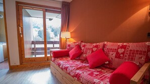 A cozy room with a wooden sofa, red cushions, and a large window with a view of trees. - Ski-in/ski-out & foot of the slopes, 3rd floor, view ski slopes, balcony, tv, ski locker, 36m² (Valmorel)