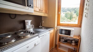 A compact kitchen with a stove, coffee maker, microwave, and wooden cabinets. - Ski-in/ski-out & foot of the slopes, 3rd floor, view ski slopes, balcony, tv, ski locker, 36m² (Valmorel)