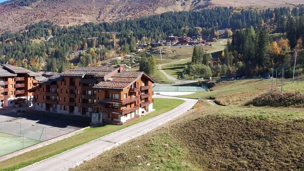 A cluster of traditional wooden buildings with balconies, set against a backdrop of mountains and a clear sky. - Ski-in/ski-out & foot of the slopes, 3rd floor, view ski slopes, balcony, tv, ski locker, 36m² (Valmorel)