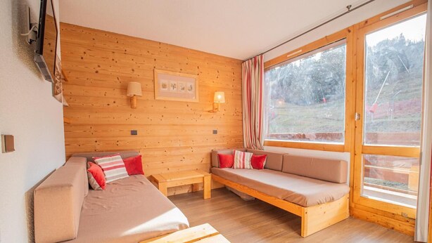 Una habitación acogedora con una pared de madera, un sofá, un banco y un amplio ventanal con vistas al exterior.