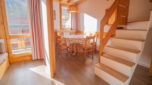 Una habitación acogedora con una escalera de madera, un comedor con mesa y sillas, y una ventana con cortinas.