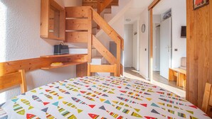 Una habitación con una escalera de madera, una mesa redonda con motivos de peces coloridos y un banco de madera.