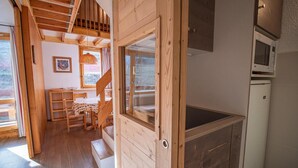 Interior de madera con cocina, comedor y escalera que sube a un nivel superior.