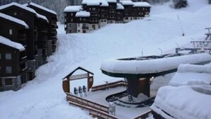 Un lodge cubierto de nieve con varias construcciones, una estructura circular central y un telesilla al fondo.