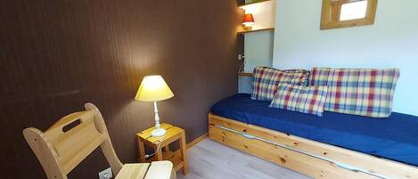 A small room with a bed, a wooden chair, a nightstand with a lamp, and a mirror on the wall.