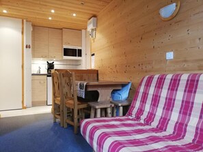 A cozy cabin interior with a wooden dining area, a kitchenette, and a striped sofa. - 200m from ski slopes, 4th floor, view panoramic, balcony, tv, ski locker, 24m², Valmorel (Valmorel)