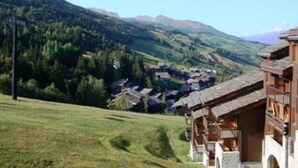 Ein traditionelles Chalet mit Steinaußenwand und Holzbalken, gelegen an einem Hang mit Blick auf ein Tal und ferne Berge.