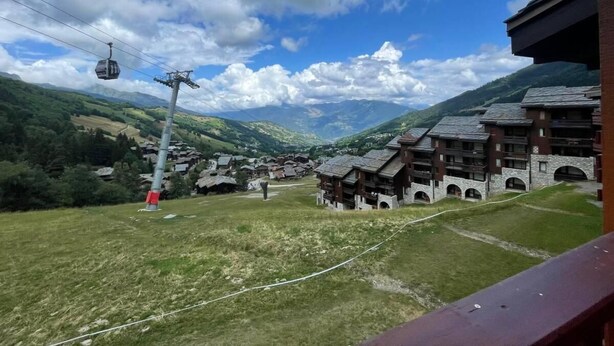 Ein Bergort mit traditionellen Chaletbauten, einer Seilbahn und Blick auf die umliegenden Hügel.