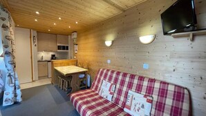 Ein gemütliches Cabin-Interieur mit Holzbalkendecke, einer Küchenzeile, einer Couch und einem an der Wand montierten Flachbildfernseher.