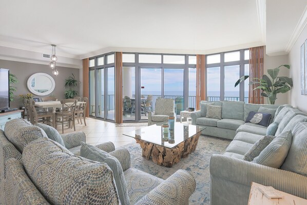 A spacious living room with a large glass door leading to a balcony, a round dining table, and a comfortable seating area with sofas and a coffee table. - The Oasis at Orange Beach, formerly known as Phoenix West II, Unit 1703 (Orange Beach)