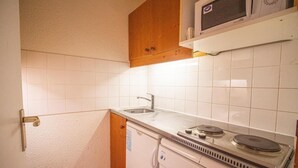Eine kleine Küche mit Spüle, Herd, Mikrowelle und Holzschränken.