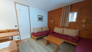 Ein Zimmer mit Holzboden, einem roten Sofa, einem Holztisch und einer weißen Tür.
