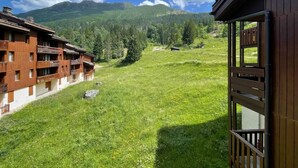 Ein Hotel mit Holzfassade, einem Balkon und Blick auf ein grünes Feld sowie Berge im Hintergrund.