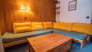 Et hyggeligt rum med trævæg, en sofa med gule puder, et træbord og et billede på væggen.
