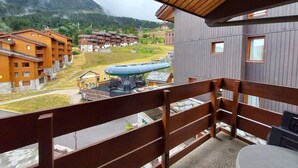 En balkon med udsigt over et bjergrigt område, en stolelift og flere bygninger.