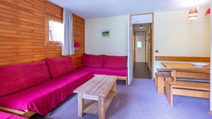 A cozy room with a wooden wall, a red sofa, a wooden table, and a bench. - 50m from shops, 2nd floor, view mountain, balcony, tv, ski locker, 35m², Valmorel (Valmorel)
