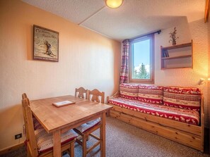 A cozy room with a wooden table and chairs, a bench with patterned cushions, a window with curtains, and a wall-mounted shelf with a plant. - 100m from shops, 2nd floor, view valley, balcony, tv, ski locker, 22m², Valmorel (Valmorel)