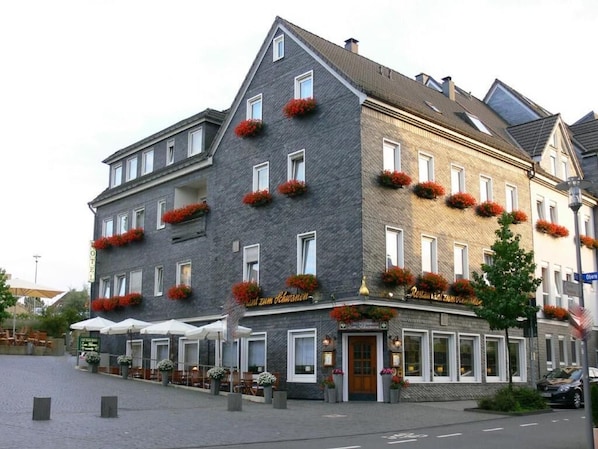 Un hotel de varios pisos con fachada de piedra, múltiples ventanas y balcones con flores.