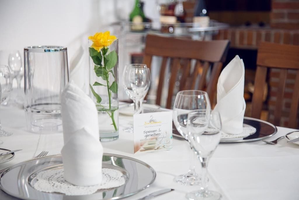 Ein Esstisch mit Geschirr, klarem Glas und einer Vase mit einer gelben Blume, sowie einer Speisekarte.