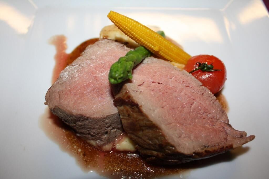 Un plato con rodajas de carne, un elote y un tomate cherry.