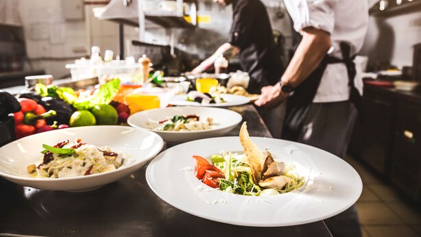 A chef preparing food in a kitchen with various dishes and ingredients on the counter. - Hotel-Restaurant Zum Schwanen (Wermelskirchen)